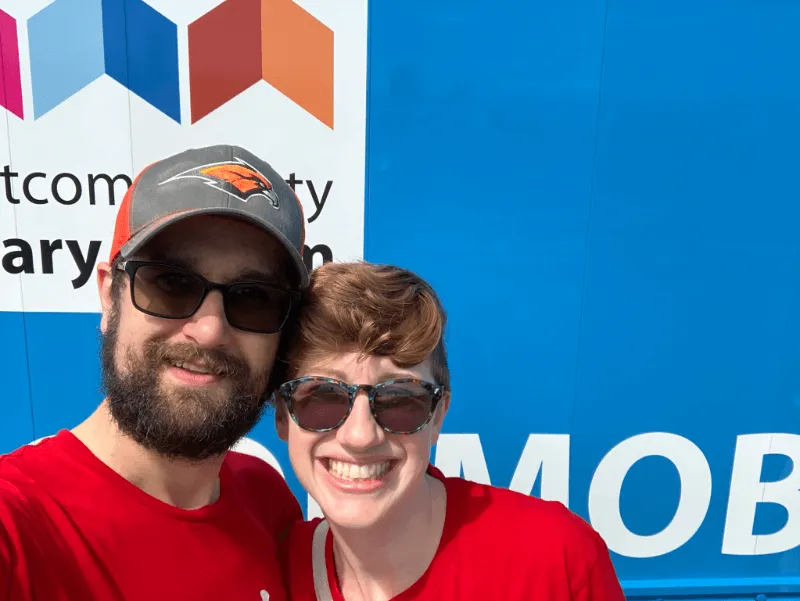 A man and a woman smiling in front of the Whatcom County Library Services book-mobile
