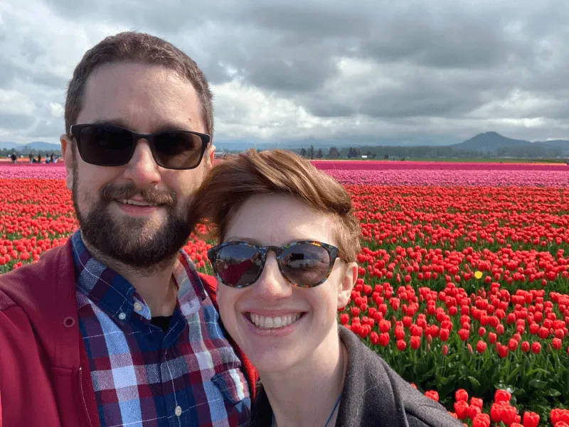A man and a woman smiling in front of countless rows of red, pink, and purple tulips
